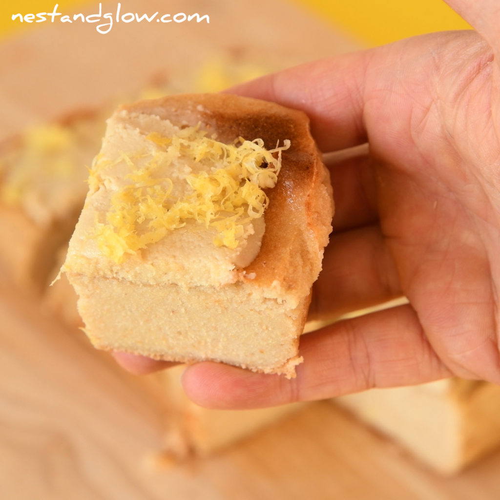 holding a slice of healthy quinoa tray bake cake that is topped with cashew frosting and lemon zest.