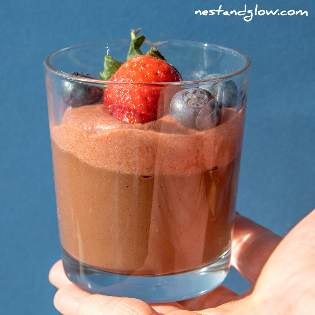 holding a single portion of berry chocolate mousse that's good for you with just 4 ingredients. suitable for vegan, gluten free, nut free and whole food diets.